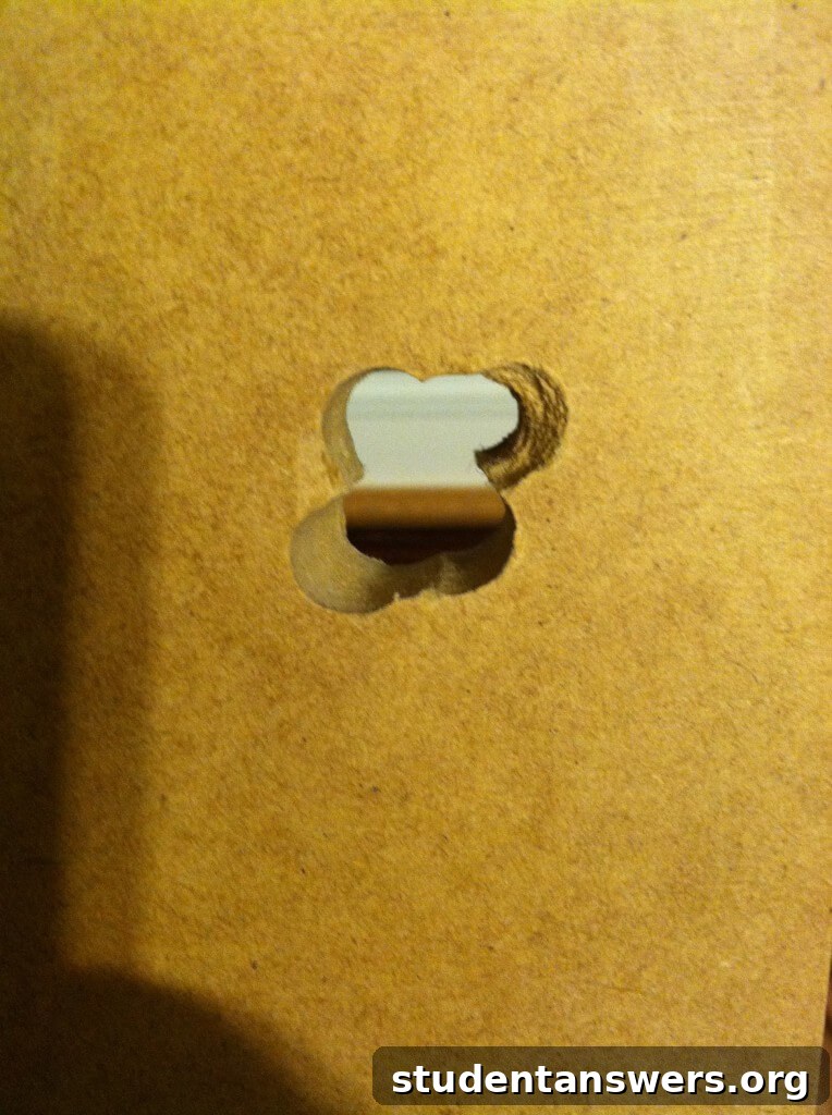 A close-up of a roughly drilled hole in the corner of the wooden desk board.