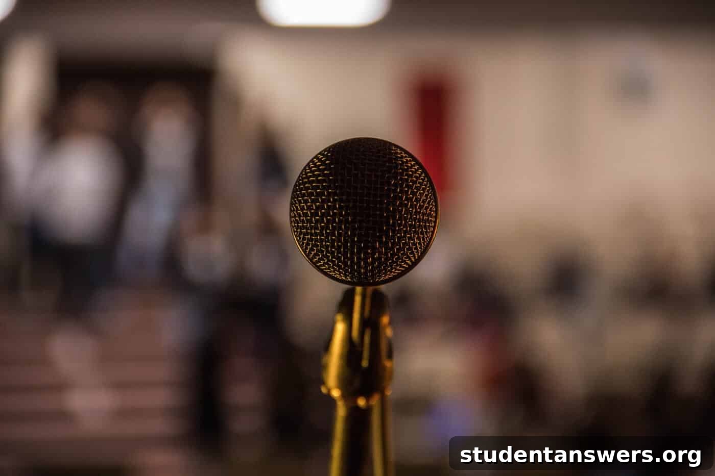 A close-up of a professional microphone on a stage with a blurred, ambient background.