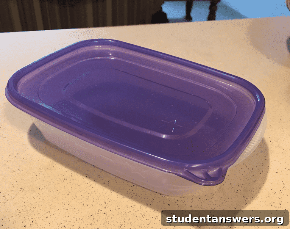 A stack of uniform, black meal prep containers with clear lids, showing portioned meals inside.