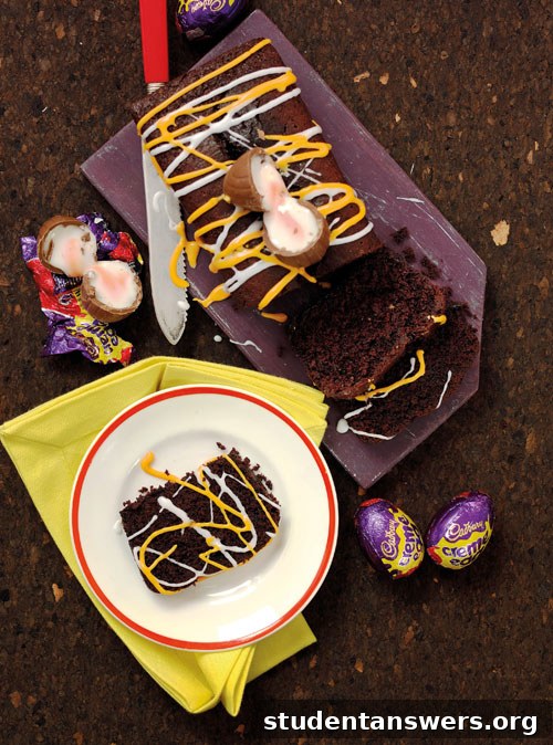 A slice of chocolate loaf cake with white and orange icing, topped with a gooey half of a Cadbury Creme Egg.