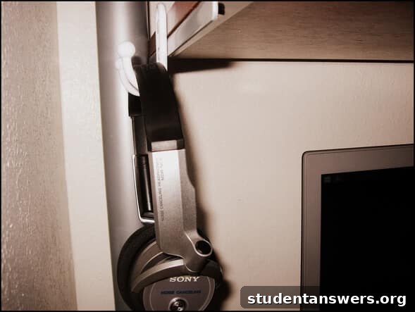 Headphones hanging from a coat hook mounted under a desk.